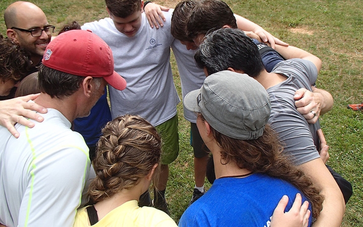 A group of people stand in a circle with their arms around each other's shoulders.